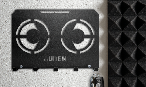 Metall veggmontert nøkkelholder med geometrisk utskjæring og personlig navn, montert på en strukturert vegg