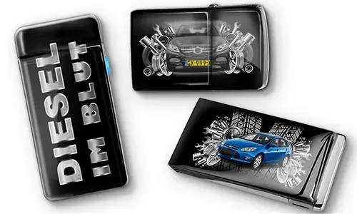 Drei schwarze Feuerzeuge mit Auto-Motiven und metallischen Akzenten. Eines trägt den Text „DIESEL IM BLUT“, die anderen zeigen rote und blaue Autos mit mechanischen Motiven. Ein sportlicher Ton wird vermittelt.
