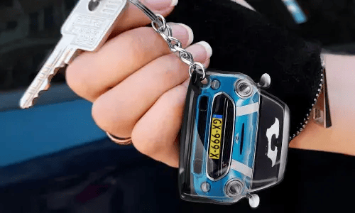 Ręka trzymająca brelok w kształcie niebieskiego samochodu z detalicznym przodem