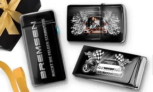 Elegante schwarze Feuerzeuge mit Auto-Designs. Eines zeigt eine Familie in einem Auto, ein anderes ein blaues Auto mit karierten Flaggen. Daneben liegt eine Geschenkbox mit goldener Schleife.