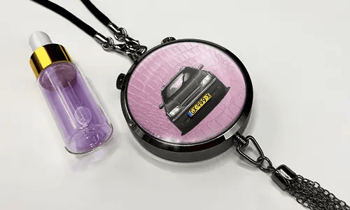 Anhänger mit rosa Hintergrund und weißem Sportwagen, daneben violette Tropfflasche mit goldenem Deckel