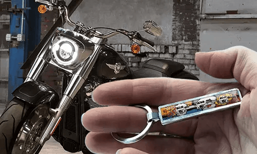Comic style metal keychain with motorcycle illustration held in hand near bike