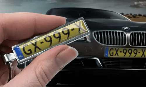 Nøkkelring i tegneseriestil med bilskilt, holdt i hånden foran en bil med matchende skilter