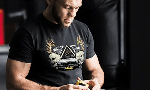 Black T-shirt with graphic of car, skulls, pistols, golden wings, and starry triangle background