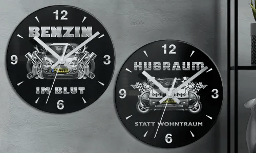 Two black wall clocks with car illustrations and German text: BENZIN IM BLUT and HUBRAUM STATT WOHNTRAUM
